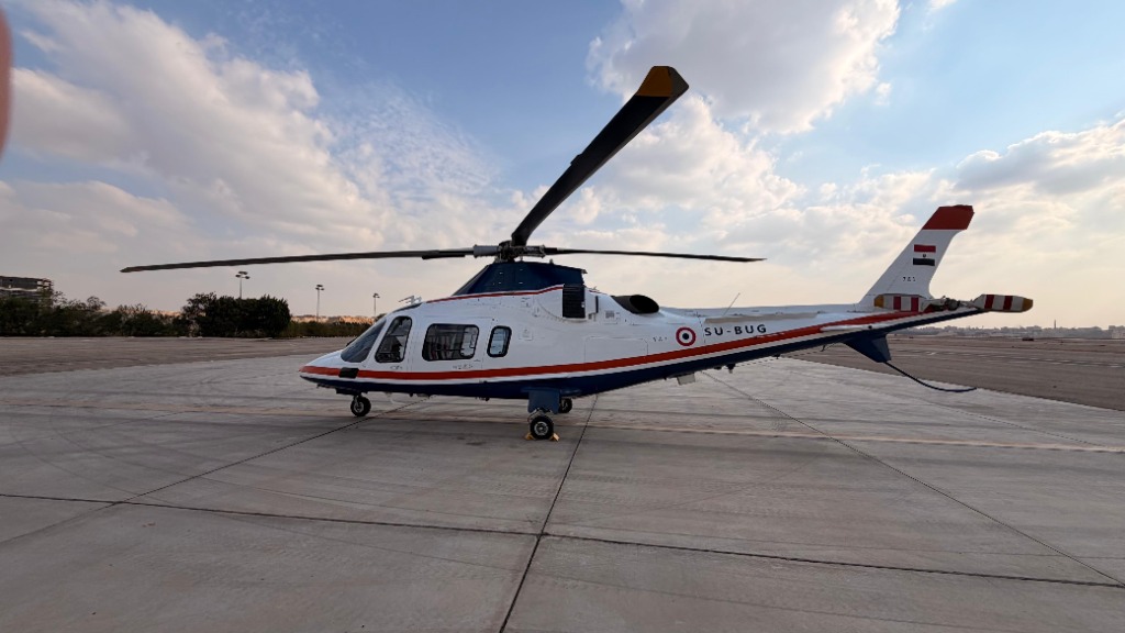 Side view of the Xtreme Sky helicopter resting on a wide concrete apron under a partly cloudy sky