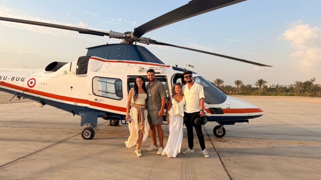 Illustrative group photo: four guests posing in front of the helicopter on the airfield apron